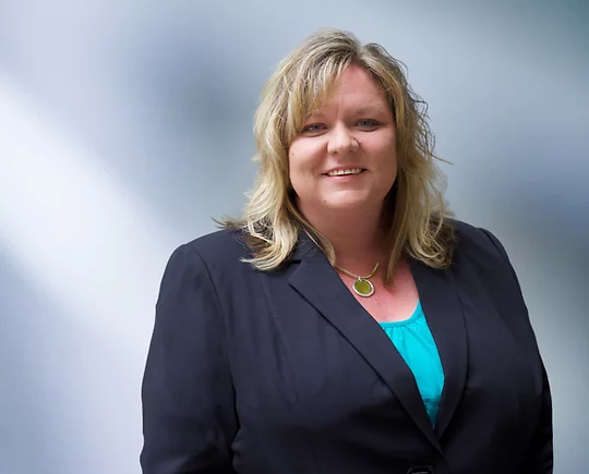 Portrait of a woman, Terry Bolyard, with long blonde hair in a dark blazer, with a blurred blue and white background.