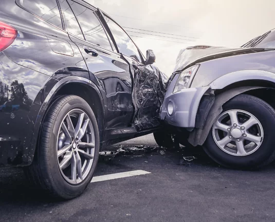 A T-bone car accident involving two vehicles in a parking lot; one car has significant damage to its front, and the other is damaged on the side where it was struck.