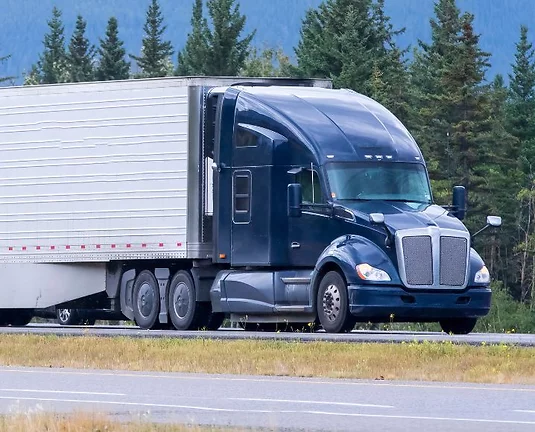 Semi-truck driving down a road with trees in the background.