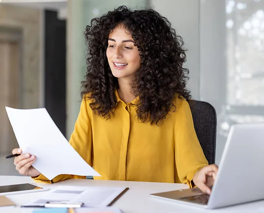 Successful and joyful woman at workplace checking financial reports and contracts. Businesswoman doing paperwork inside office, using laptop