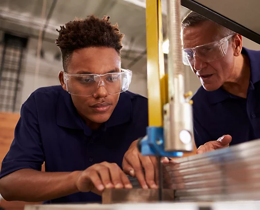 Young teenager concentrating on cutting metal while older man helps him