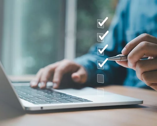 Person working on a laptop with a virtual checklist overlay, checking off items with a pen.
