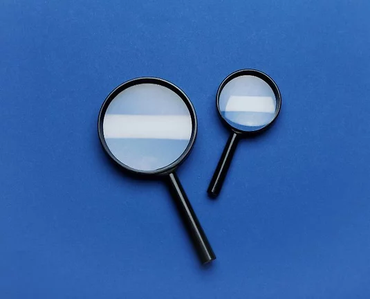 Two black magnifying glasses, one large and one small, placed on a solid blue background.