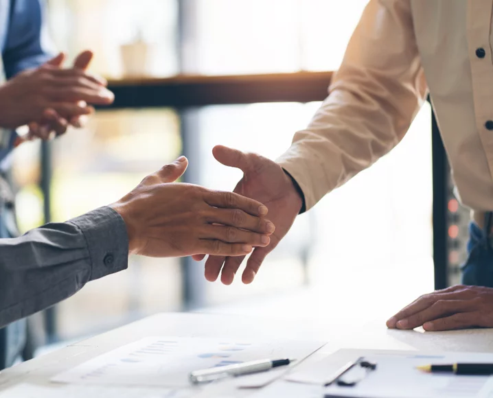 Hands shaking over contracts on table