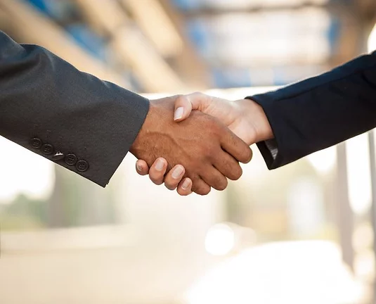 Close-up of two businesspeople shaking hands, symbolizing agreement or partnership, with a blurred office-like background.
