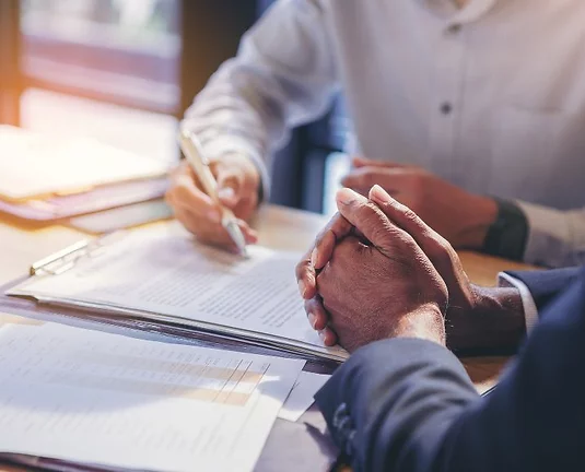 Two professionals reviewing and signing documents at a desk, suggesting a business or legal consultation.