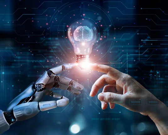 Futuristic concept showing a robotic hand and a human hand reaching toward each other with fingers nearly touching, creating a spark of light between them that forms a glowing lightbulb, symbolizing collaboration between artificial intelligence and human