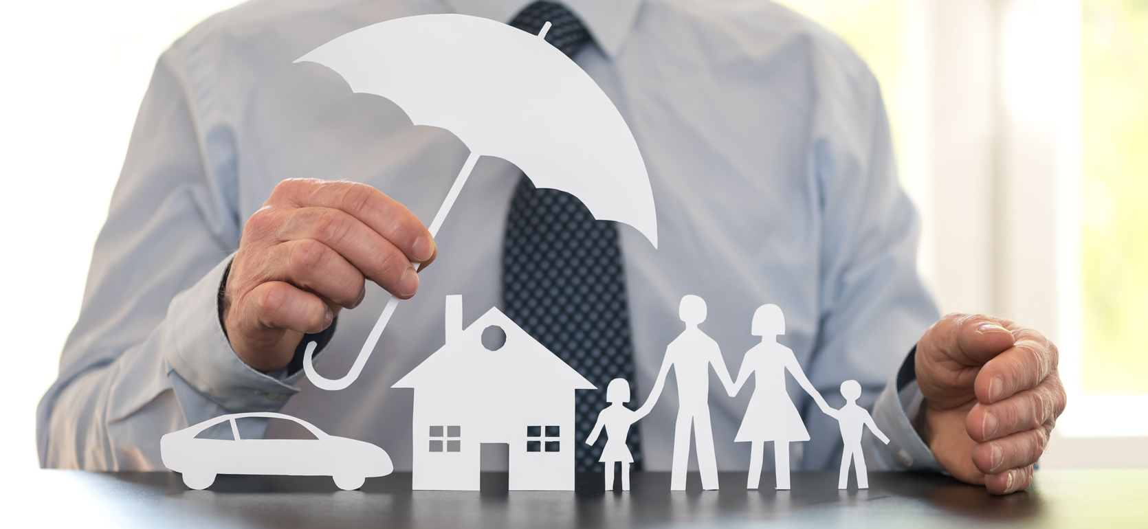Man wearing shirt and tie holds white paper cutout umbrella above paper cutouts of car, home and family members