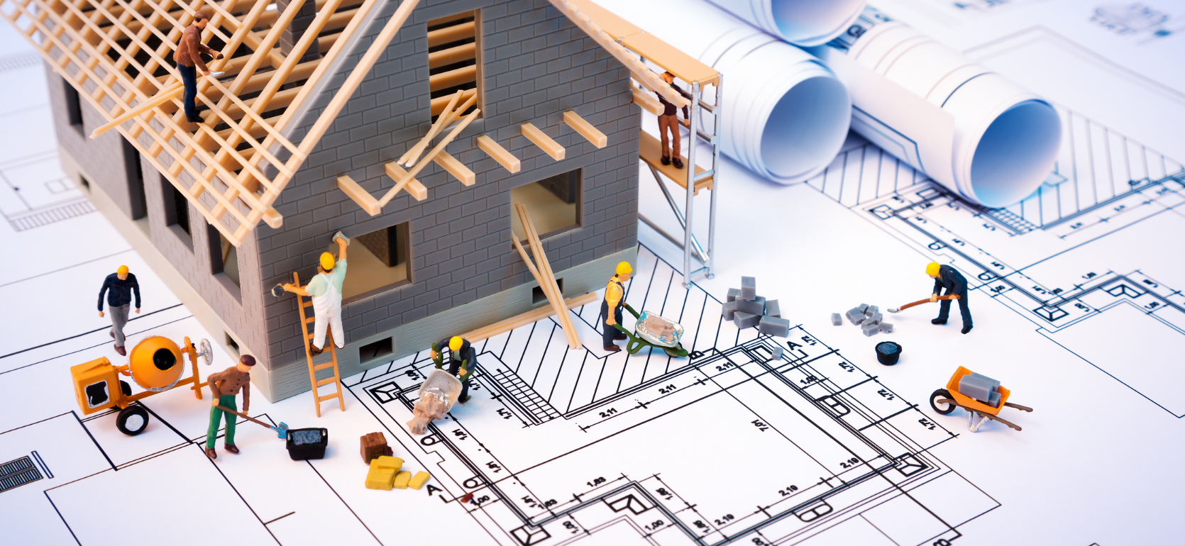 Mini construction worker toys building a house together on top of life size blue prints
