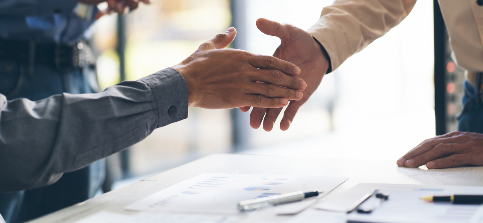 Hands shaking over contracts on table