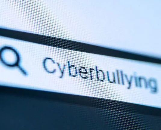 Close-up of a computer screen showing the word “Cyberbullying” typed into a search bar, with a magnifying glass icon indicating a search function.
