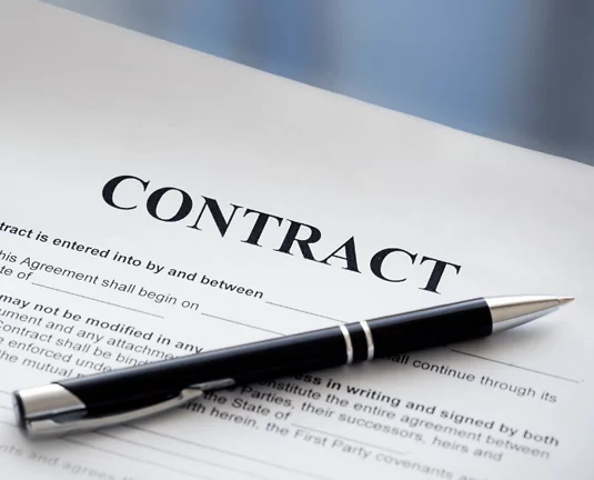 A close-up of a contract document with the word “CONTRACT” prominently displayed at the top, and a black pen resting diagonally across the paper, suggesting agreement or pending signature.