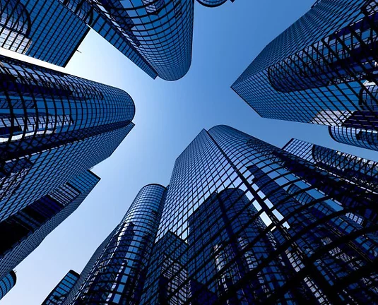 Low-angle view of modern glass skyscrapers reflecting the sky, converging toward the center with a clear blue background.