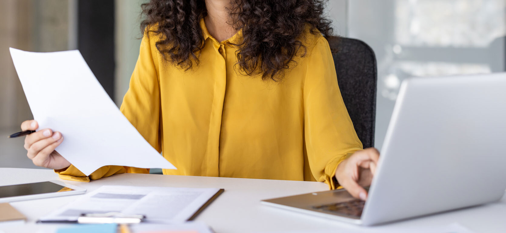 Successful and joyful woman at workplace checking financial reports and contracts. Businesswoman doing paperwork inside office, using laptop