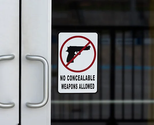 NO CONCEALABLE WEAPONS ALLOWED sign on the outside of a door on public building warning people not bring their guns inside.