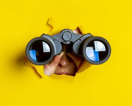 Female hand holds black binoculars on a yellow background.